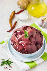 Raw chicken liver in a plate, pepper, herbs, oil. Selective focus, space for text.