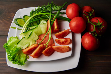 sliced tomatoes cucumbers lying on a white plate decorated with green onions standing on a dark wooden table