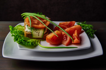 sandwich with cheese and sliced tomato cucumbers, lying on a white plate, decorated with green onions, standing on a dark wooden table