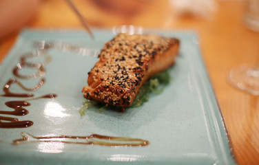 Delicious grilled salmon steak - rich omega 3 source - on a blue plate with sauce in sesame seeds in a fancy restaurant. Creative serving in a fancy restaurant 