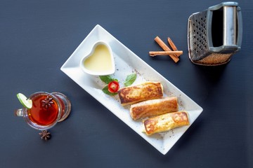 Pancakes on a white plate with tea, spices, lemon and cinnamon on a dark background