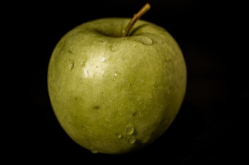 Green apple with water drops on black background