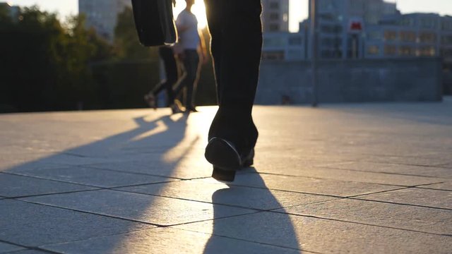 Feet of businessman with briefcase walking in city street at sunset time. Businessman commuting to work. Confident guy being on his way to office. Worker going outdoor. Front view Close up Slow motion