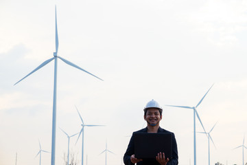 Successful engineer man standing and using computer laptop with wind turbine.