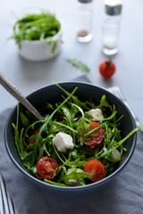 Bowl of arugula salad with tomatoes and cheese on gray wooden background. Vegetarian food concept