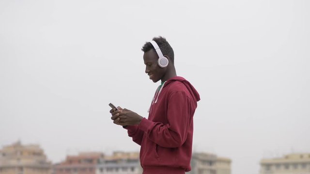 young african american guy listening music and typing on smartphone-outdoor