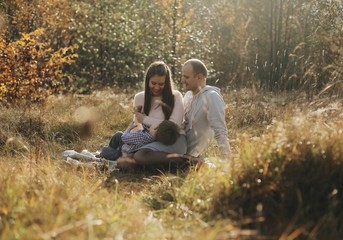 Young family sitting In long grass in autumn forest