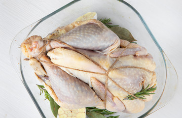 Uncooked guinea fowl in transparent glass baking dish with garlic and rosemary