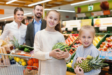 Family is standing with cart with products in the supermarket.