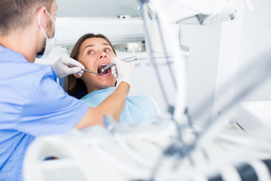 Dentist is treating woman patient which is sitting chair in clinic