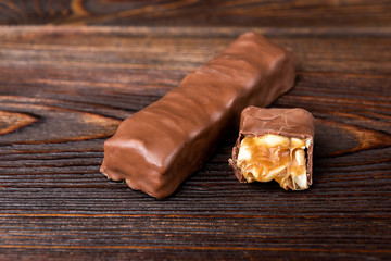 Chocolate bar with caramel and peanut on dark wooden background. 