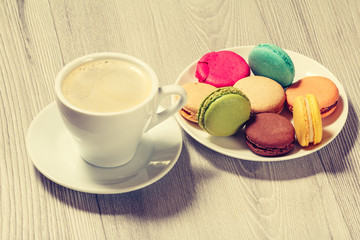 Cup of coffee and delicious macarons cakes of different color on plate