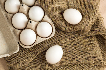 Fresh white eggs on burlap textile at rustic background with copy space. Rural still life, organic healthy food.