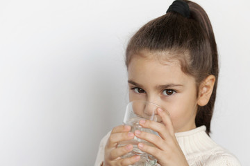 Cute child girl drinking water on white background. Pure water.