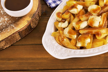 Poutine plate on a wooden background. Cooked with french fries, gravy and curd cheese. Canadian...