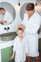 happy father making hair of cute daughter standing in bathroom