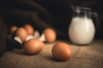 Photo of raw illuminated eggs  in kitchen with jute on dark blurry background Close-up photography of bio chicken eggs in egg box with milk in a ewer glass.