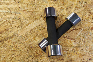 two stainless steel dumbbells with a black rubber grip on the wooden floor. dumbbells on each...