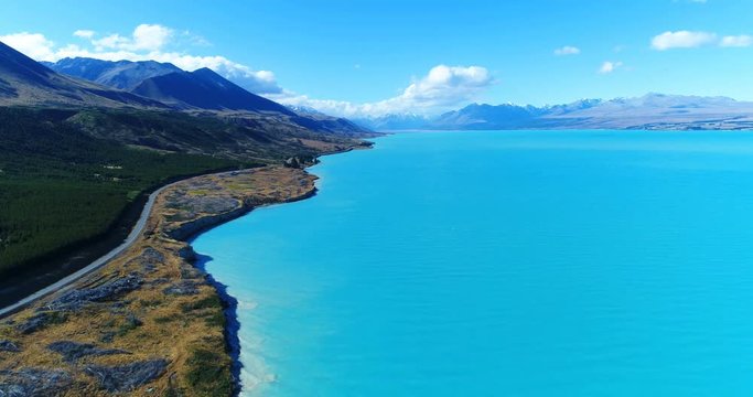 New Zealand aerial drone footage of lake Pukaki and southern alps on South Island. Road and clear blue lake and sky with Aoraki / Mount Cook National Park in background. New Zealand Tourist attraction