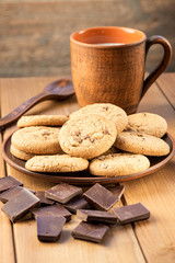 Oatmeal cookies, chocolate and a cup of milk on a wooden table.
