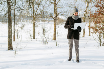 A young guy in the winter in the woods with a laptop. Freelance concept
