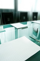 Fototapeta premium Waiting for the meeting. The crystal table set with paper pads for notes, pens and business cards reflects the curtains with vertical strips that cut the light of the large windows
