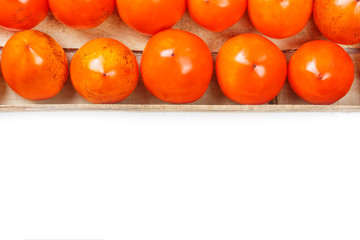 Juicy ripe persimmon in a large wooden box on a white background.