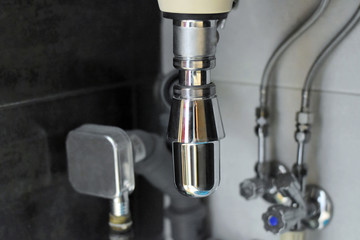Chrome sanitary elements and pipes with selective focus under bathroom sink. Sewerage system with steel fitting connector elements. Home water plumbing construction with metal siphon under basin.