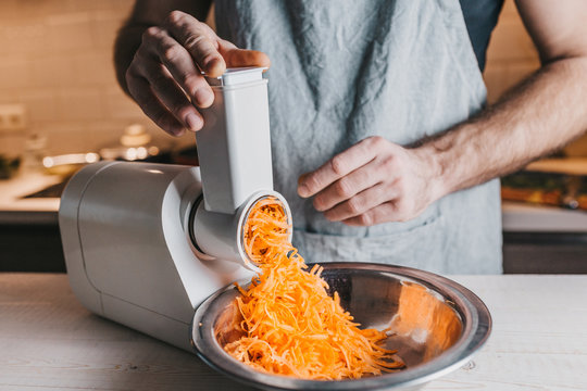 Closeup of a rough male chef hands chopping carrots on an electric meat grinder