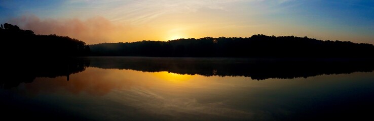 Panoramic view of the rising sun peeks over the foggy horizon at Shelley Lake Park in Raleigh North Carolina.