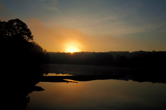 The rising sun peeks over the foggy horizon at Shelley Lake Park in Raleigh North Carolina.