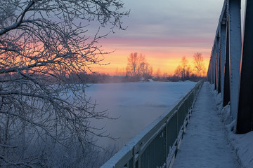 An iron bridge covered with snow goes off into the blazing sky with fire.