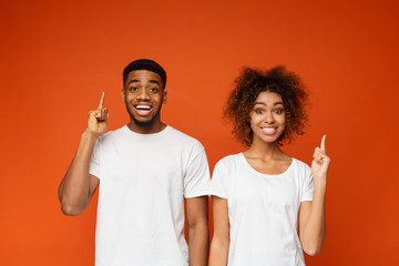 Cheerful man and woman point index fingers up