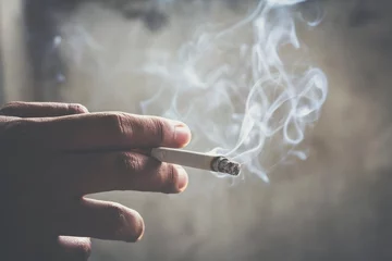 Fototapeten man holding smoking a cigarette in hand. Cigarette smoke spread. dark background © methaphum