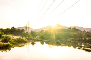 Blur background of flare light in the morning, Electricity pole with mountain in the morning, Light yellow of sunrise in winter, Beautiful flare light with landscape mountain in Thailand, Green nature