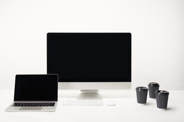 workplace with coffee to go, desktop computer and laptop with copy space isolated on white