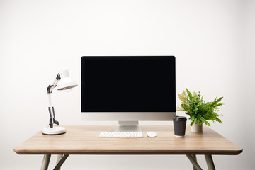 workplace with coffee to go, lamp, green plant and desktop computer with copy space isolated on white
