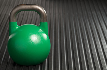 Naklejka na ściany i meble Green 24kg weight lifting kettlebell inside a gym. Copy space to the right of kettlebell.