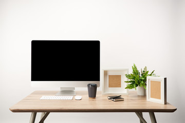 workplace with coffee to go, photo frames, plant and desktop computer with copy space isolated on white