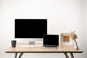 workplace with photo frame, coffee to go, dry flowers, desktop computer and laptop with copy space isolated on white