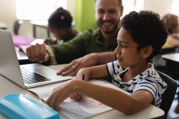 Young school teacher helping boy with study on laptop in