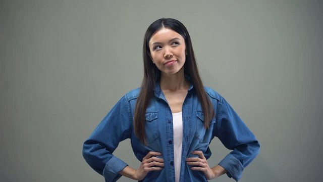 Asian woman standing on grey background, making choice between two options