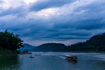 Naklejka na ściany i meble Sunset at mekong river. Blue hour with a lot of clouds. Some boats in the river. Cloudy scene in luang prabang, laos