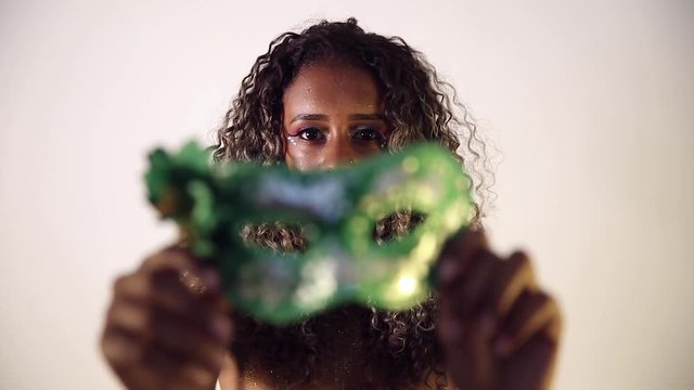 Beautiful Brazilian black female model posing in carnival mask with bright makeup and gren lipstick.