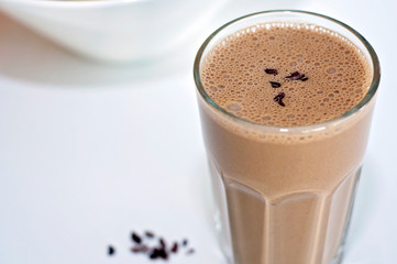 A delicious and healthy coconut-banana-chocolate smoothie on a white table, cacao nibs sprinkled on top.