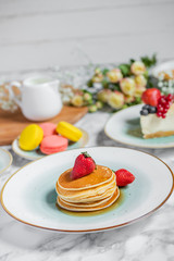 pancakes with tea, cheesecake and biscuits on a marble table with flowers