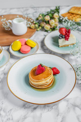 pancakes with tea, cheesecake and biscuits on a marble table with flowers