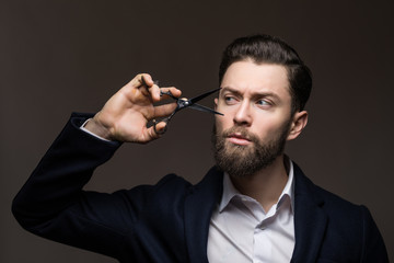 Bearded hipster man hipster barber with beard and moustache in shirt holds scissors near face in...