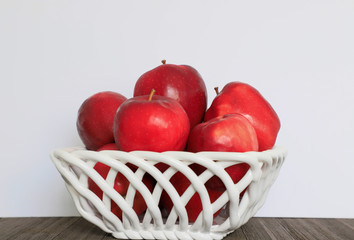 Large red apples from the home garden lie in a white wicker ceramic in a vase on a white background