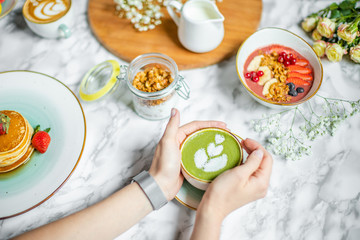 green tea latte in the hands of a girl on the table with oatmeal and flowers